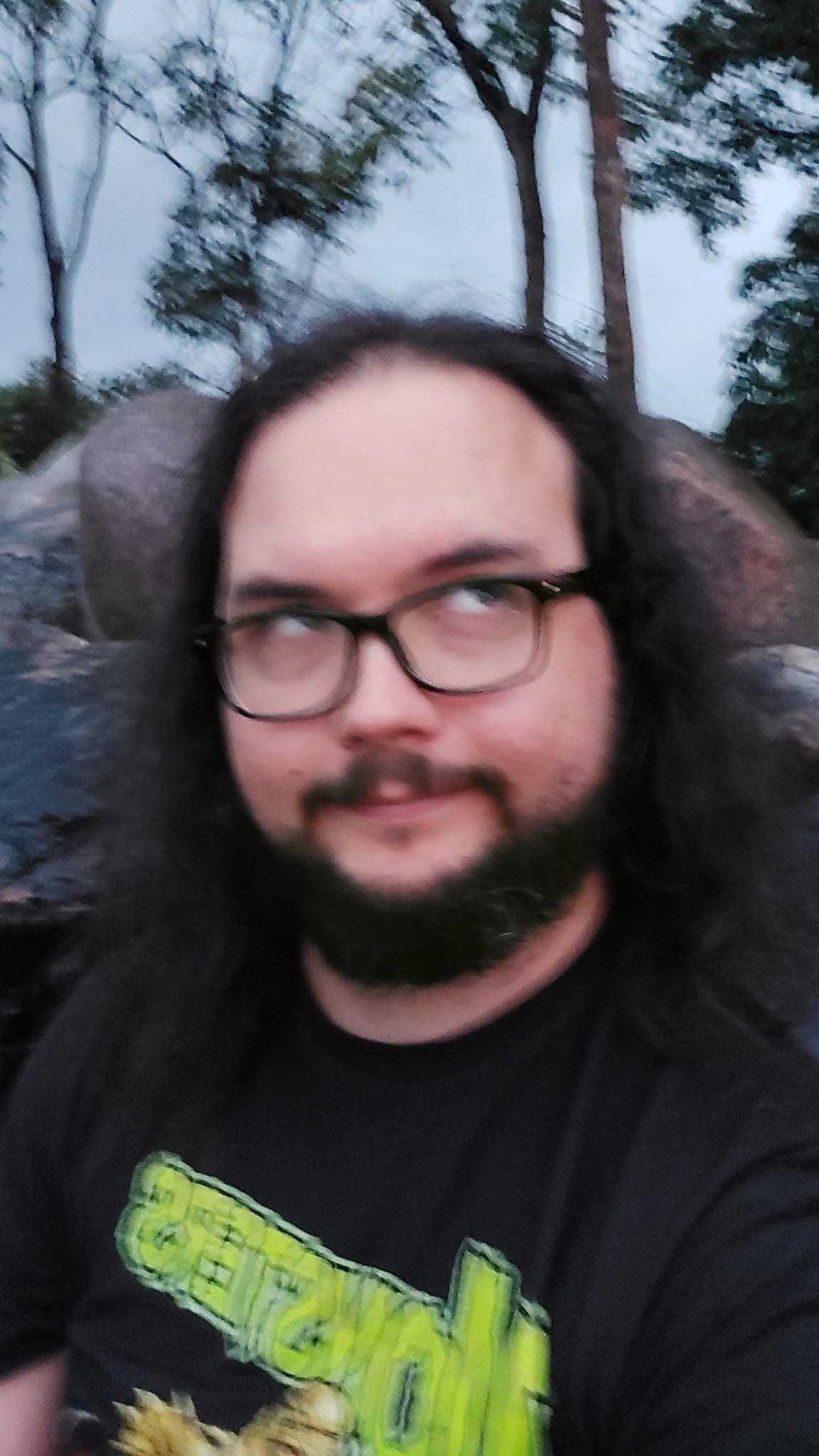 A man with long dark hair and a beard is at a sandy beach with a granite boulder breakwater, photo 3